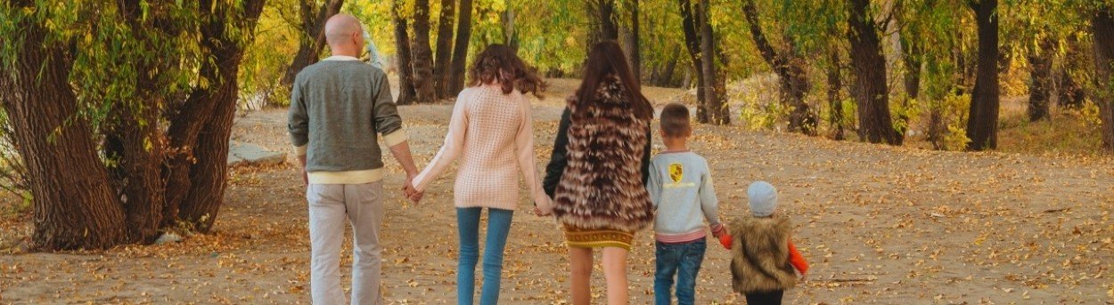 A family group holding hands and walking in a forest with their backs to the camera