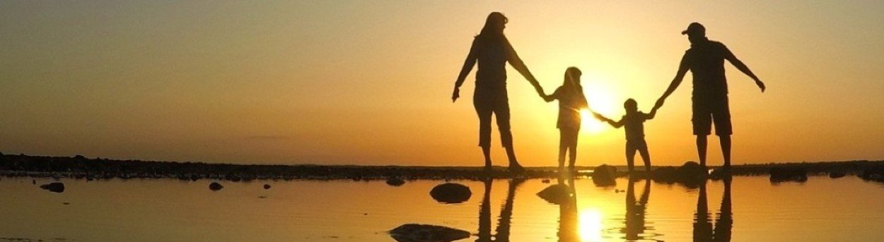 Silhouette of a family of four holding hands by the sea at sunset