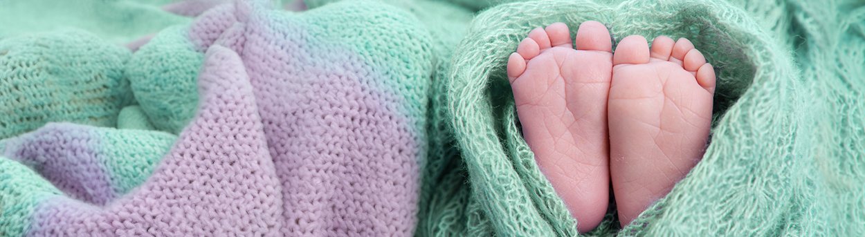 Green and lilac soft blanket wrapped in a love heart shape around a pair of tiny baby feet