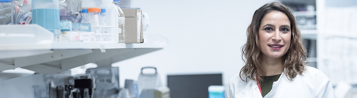 Lily researcher in a white lab coat standing at a bench full of research equipment