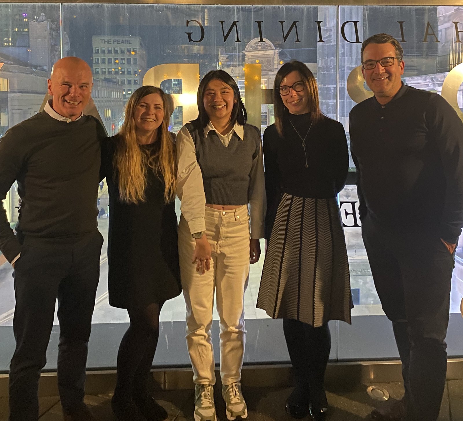 A group of five people standing in a restaurant window with a cityscape behind