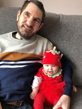 Chris sitting on the sofa with his arm around baby daughter Winter who is laughing