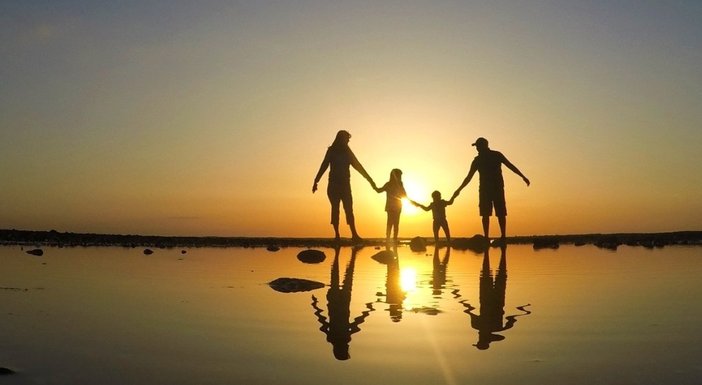 Silhouette of a family of four holding hands by the sea at sunset