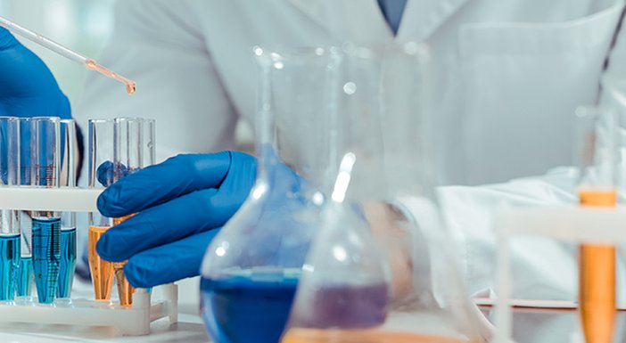 Lab technician wearing blue gloves, using a pipette to put blue or yellow liquid into a rack of test tubes