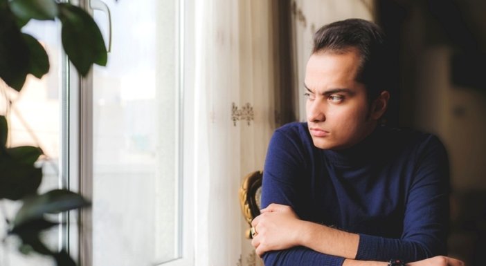 A young man looking worried stares out of the window