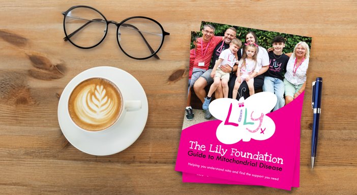 Overhead of the Lily Guide to mitochondrial disease on a table with a coffee cup and pair of glasses