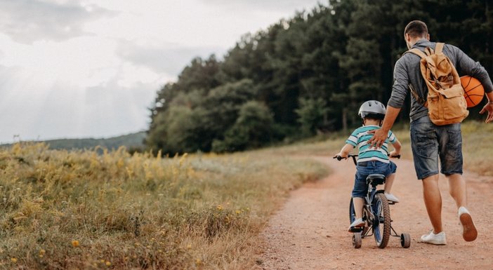 A man walking and supporting his young son on his bicycle