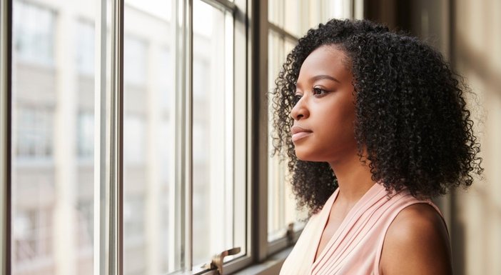 A young woman with dark curly hair staring out of a window