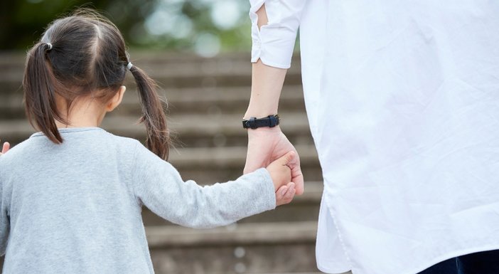 An adult in a white coat holding the hand of a small child as they climb some steps outdoors