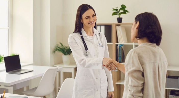 A young female doctor with a stethoscope round her neck smiling and shaking the hand of a female mito patient