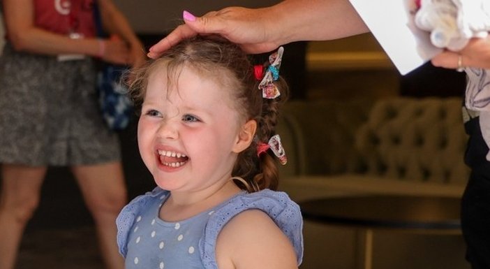 An adult places a hand protectively on the head of a young girl with mito