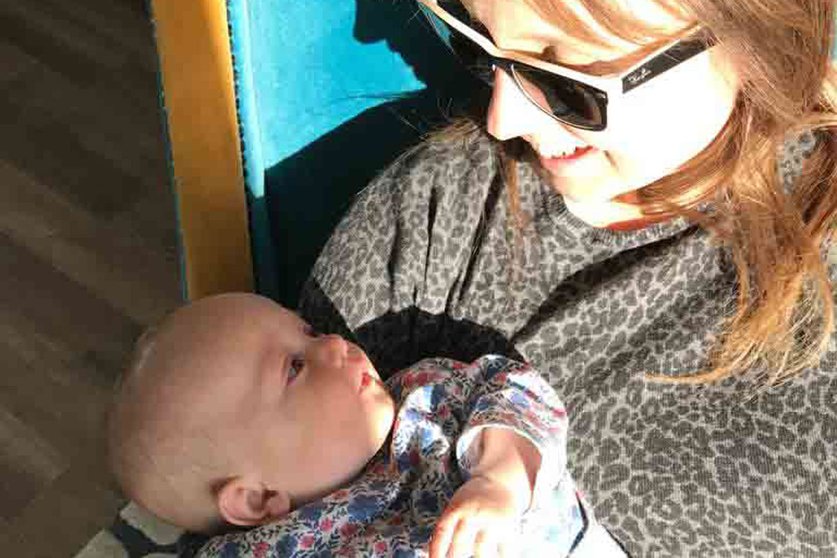 A head shot of a women in sunglasses looking down at a baby in her arms