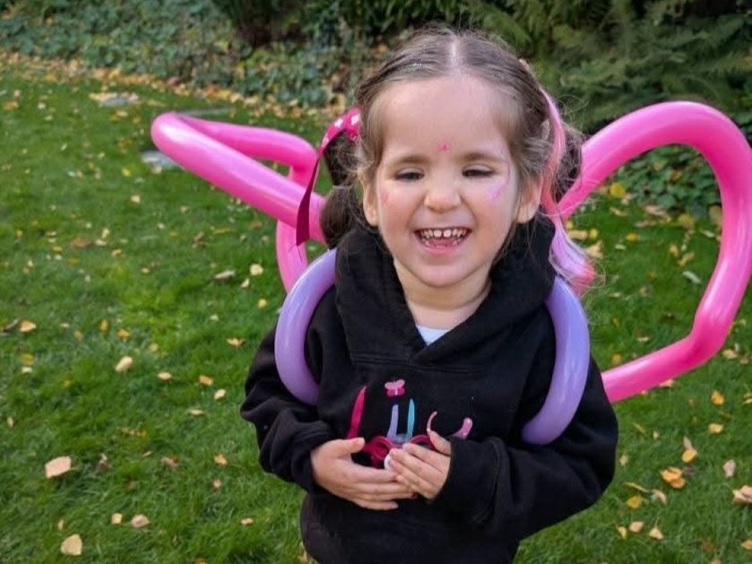 A young girl smiling and wearing a Lily Foundation top and pink wings made from balloons