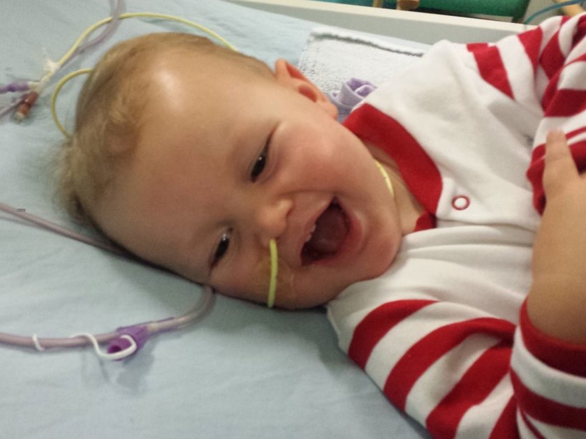 A baby wearing a red and white stripey top lying in a hospital bed with tubes around him