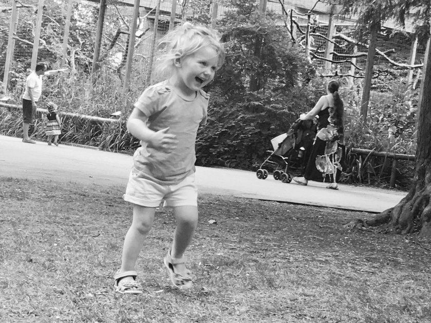 Black and white image of a blonde-haired toddler running through a park laughing