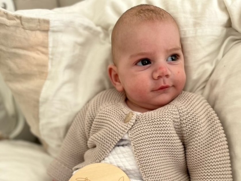 Baby Otto wearing a cream cardigan and lying on a bed