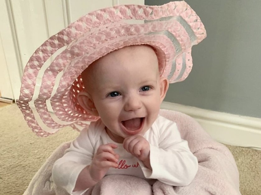 A baby wearing a large pink hat and wrapped in a towel laughing