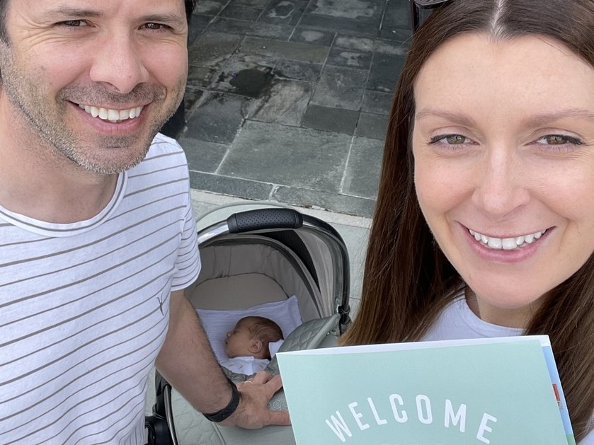 A proud mother and father standing in front of their newborn baby in a pram outside