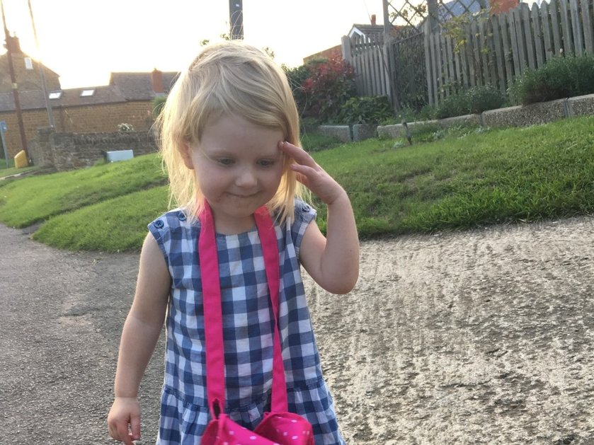 Young mito patient Grace wearing a blue check dress and sweeping away her blonde hair from her face