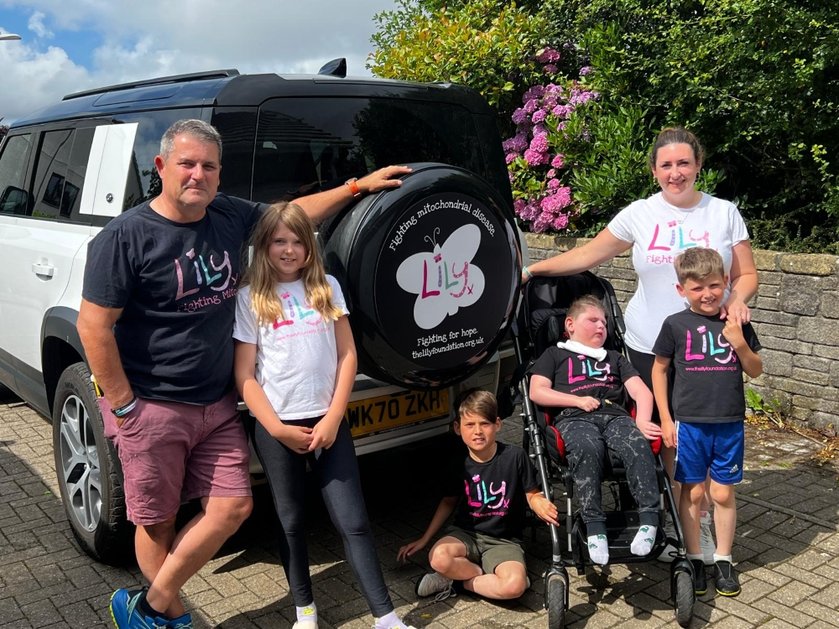 A family wearing Lily Foundation tops standing together behind a Land Rover
