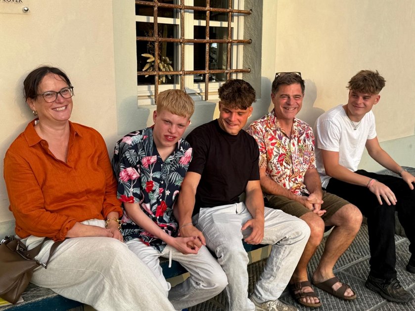 Arthur and his family sitting on a bench against a wall smiling
