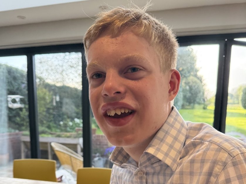 Close-up of a young mitochondrial disease patient sitting in a kitchen with a garden behind