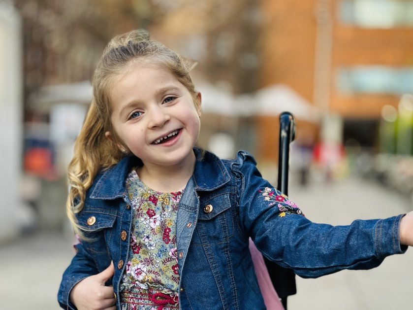 A young girl in a denim jacket with long blonde hair smiling in her buggy