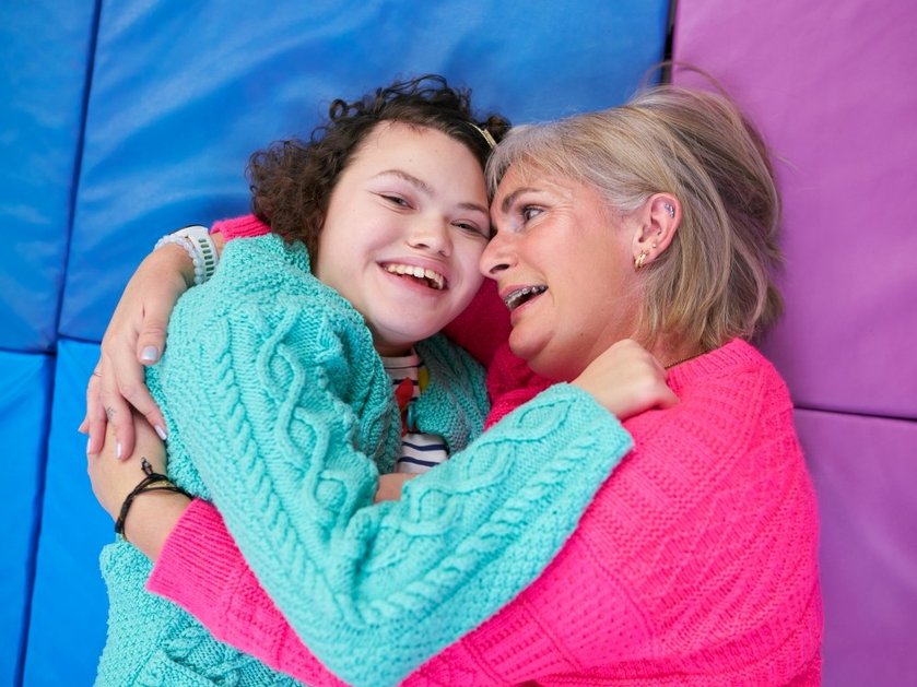 A mother lies on a mat embracing her daughter who has mitochondrial disease