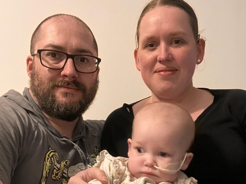 A mother and father proudly hold their baby daughter and smile at the camera