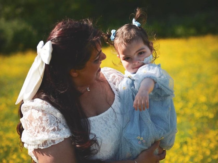 A lady in a white dress with long dark hair holding a young girl closely and looking at her