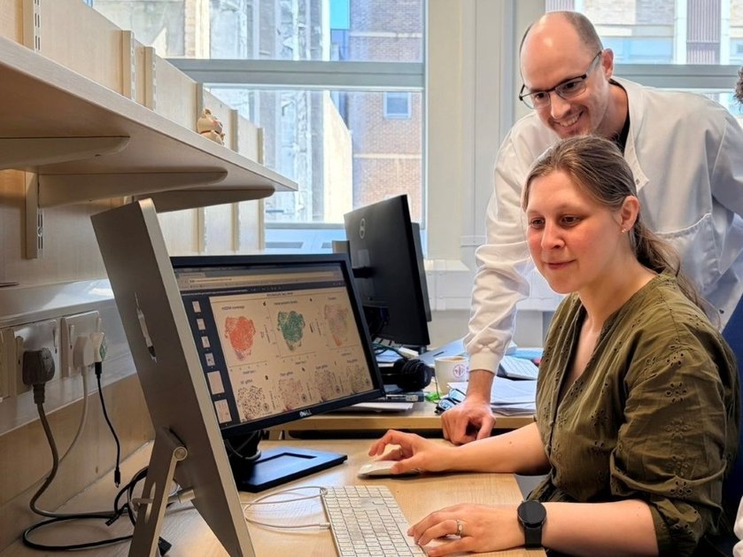 A researcher at a desk looking at a monitor with another researcher standing behind