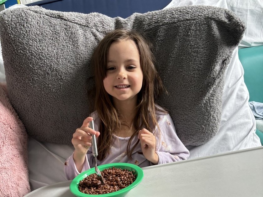 Young mito patient Matilda sitting up in bed with a large bowl of coco pops on a tray in front of her