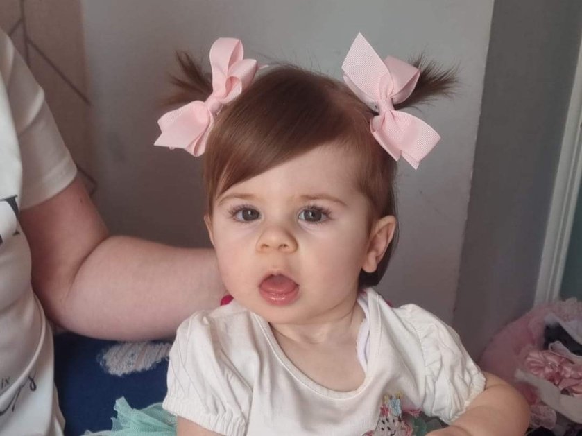 A young mito patient with dark hair and pink bows looking at the camera with her mouth open