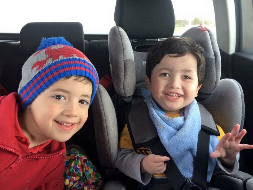 A young mito patient in a car seat smiles as an older child leans into shot