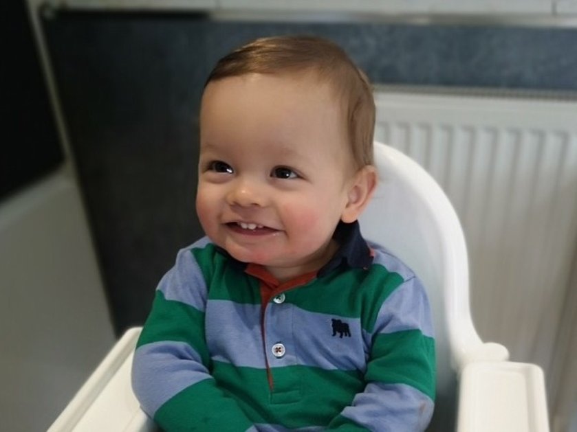 A young boy sitting in a highchair wearing a blue and green stripy top and smiling
