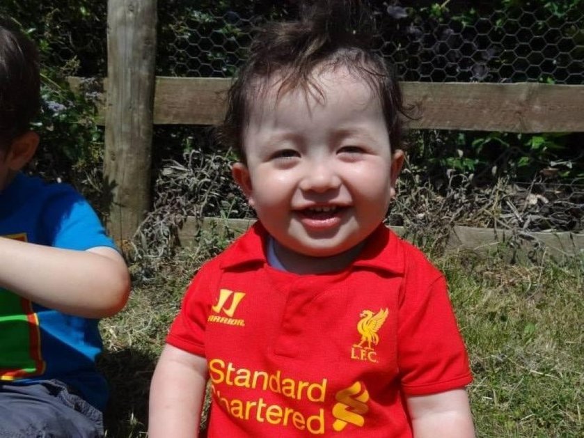 A toddler mito patient in the garden wearing a Liverpool football shirt and smiling