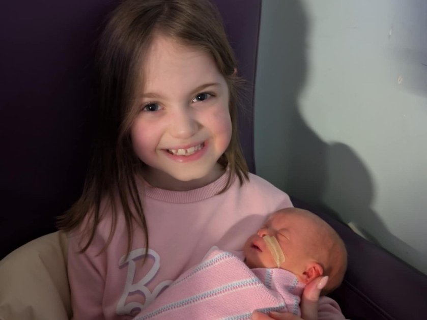 Older sister Phoebe smiling and holding tiny baby Connie in her arms