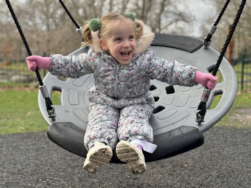 A young mito patient in a onesie sitting on a swing laughing