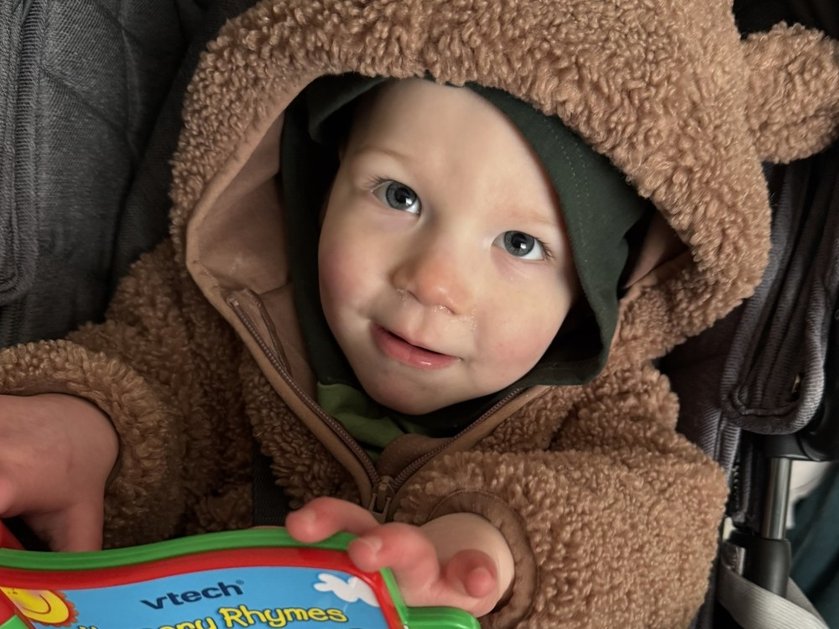 Close-up of a young mito patient wearing a brown onesie and holding a picture book
