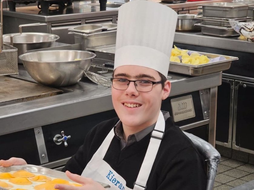 A young mito patient in a large-scale kitchen wearing a chef's hat and smiling