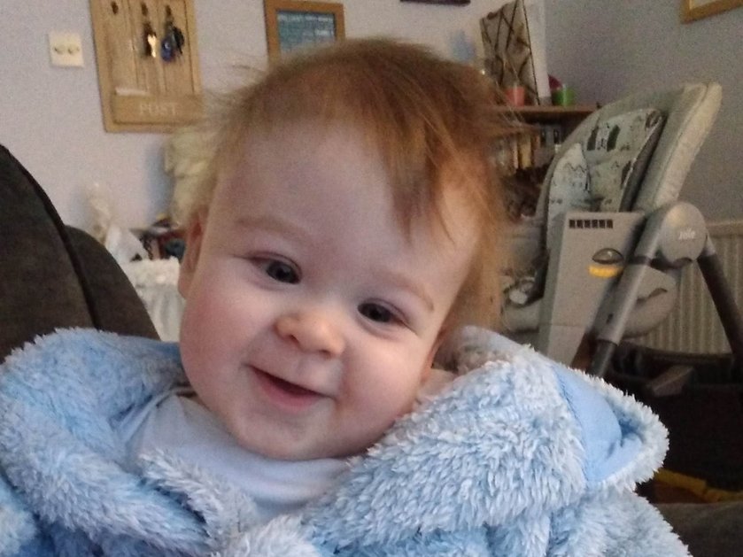 A baby with mitochondrial disease wrapped up in a blue dressing gown