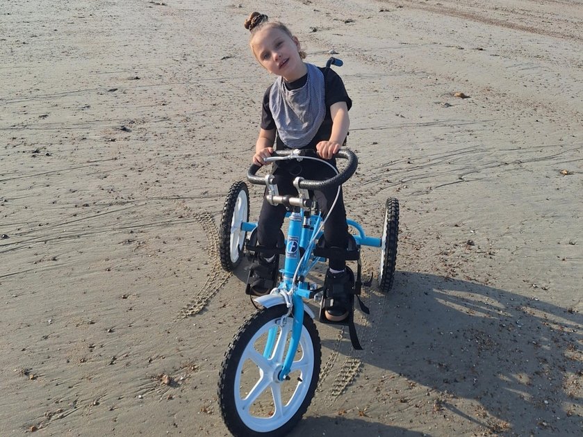A young mito patient riding a 3-wheel bike on a beach