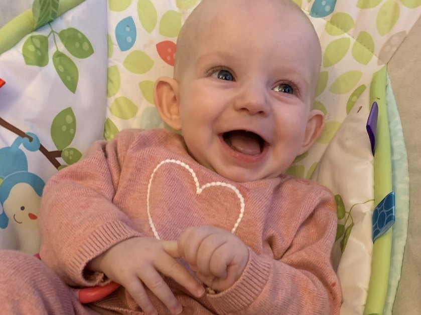 A baby lying down laughing at the camera