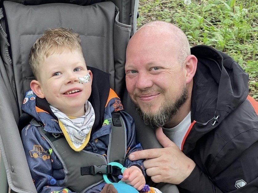 A father with his hand protectively on his son's arm smiling at the camera