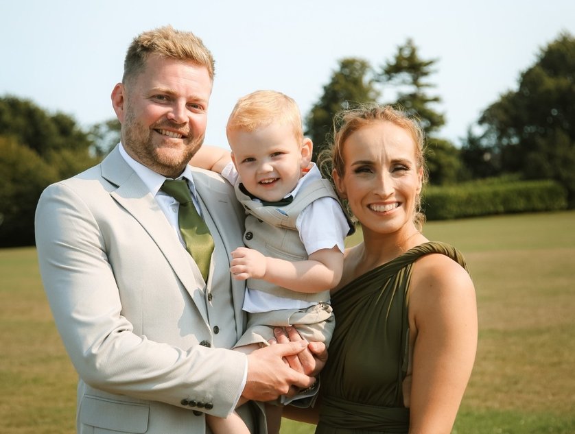 A young couple dressed in smart clothing standing outdoors and holding a young boy