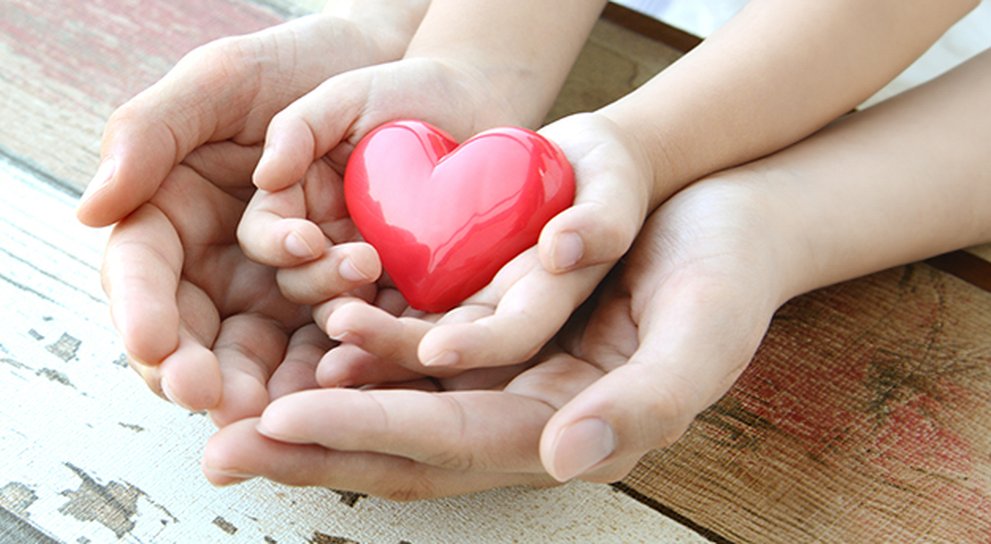Child's cupped hands holding a red heart, nestled within cupped adult hands