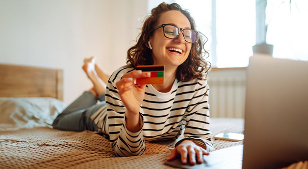 Smiling young adult with bank card in her hand at her laptop