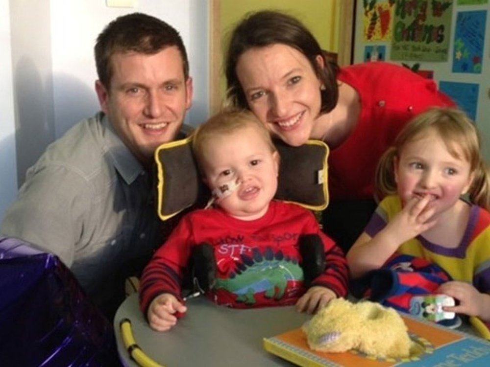 Mum, Dad and two children. Their son has mito and is in a wheelchair with a feeding tube in his nose