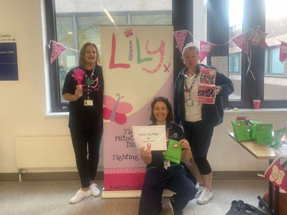 Three people standing in front of a Lily banner holding merchandise