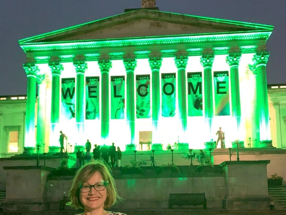 A lady standing in front of the Portico Building at UCL which is lit up green